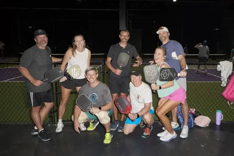 Group of people posing with pickleball paddles, outdoors at night - Pickle-Pins