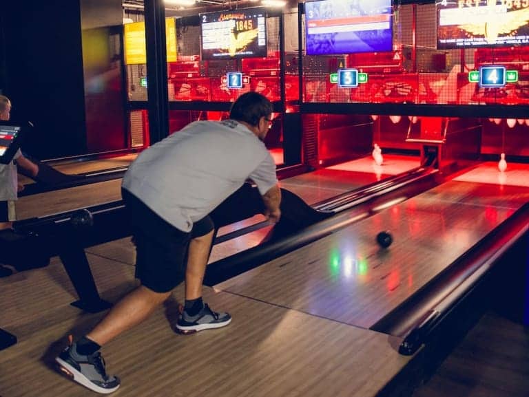 Man bowling in a brightly lit, modern bowling alley at Pickle-Pins