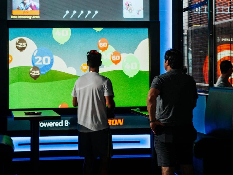 Two people playing an interactive golf game on a large screen at Pickle-Pins