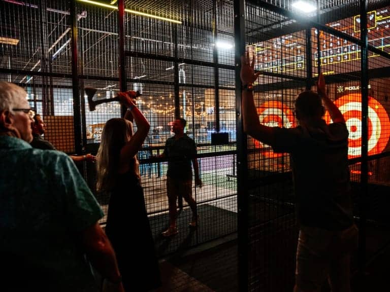 People participating in axe throwing, view from behind, at Pickle-Pins