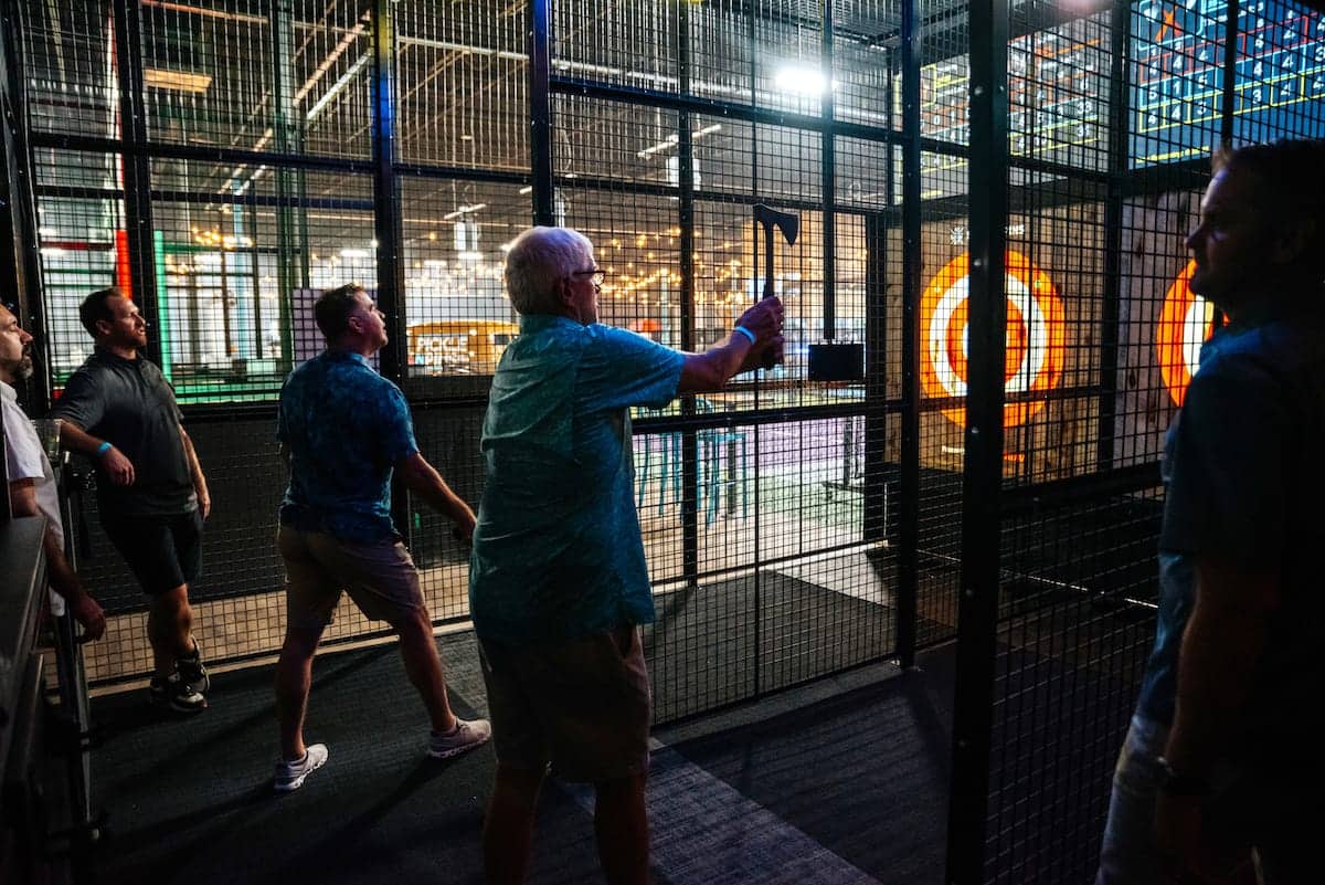 People playing axe throwing in a caged lane at Pickle-Pins