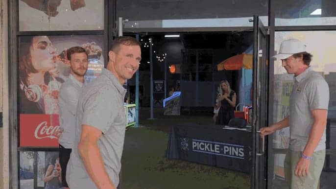 Smiling man standing near a Pickle-Pins entrance sign