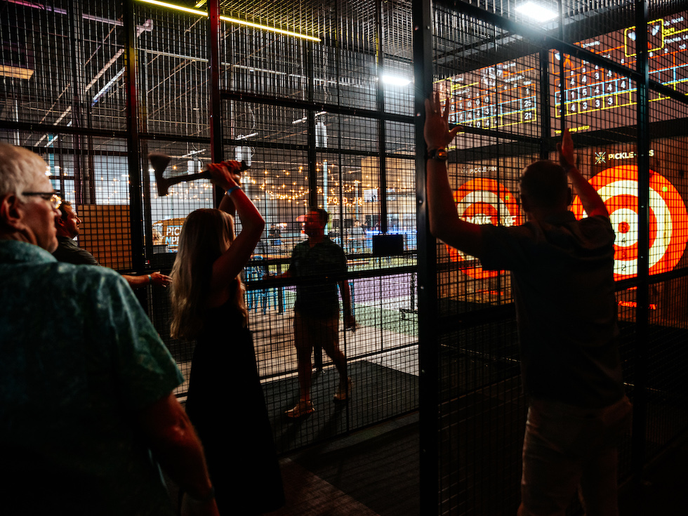 People participating in axe throwing, view from behind, at Pickle-Pins